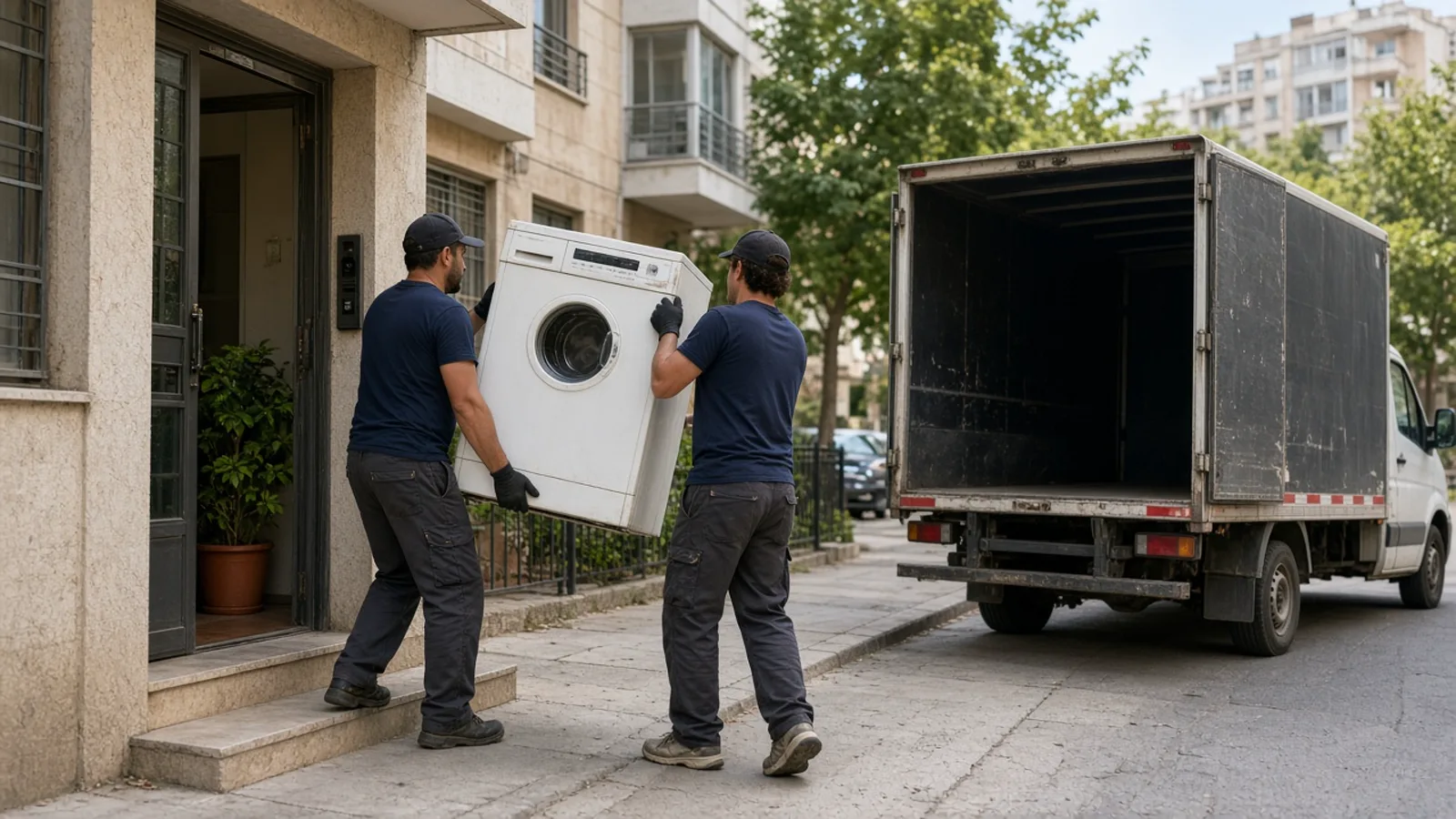 שני מובילים מוציאים מכונת כביסה ישנה מפתח בניין ישראלי אל רכב קטן, פינוי מוצר חשמל כבד בזהירות ובלי מאמץ מיותר.